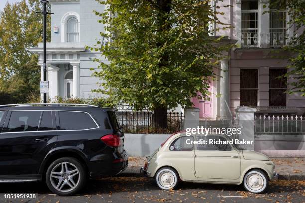 Large 4x4 SUV car parked behind a much smaller FIAT 500 among autumn leaves on Elgin Crescent in Notting Hill, on 7th October 2018, in London,...