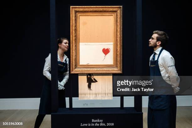 Sotheby's employees view 'Love is in the Bin' by British artist Banksy during a media preview at Sotheby's auction house on October 12, 2018 in...