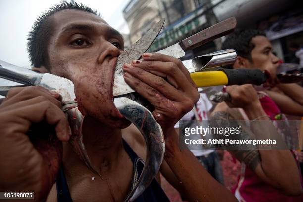 Devotee of the Chinese shrine of Ban Tha Rue, pierces his cheeks with swords during a procession at the Vegetarian Festival on October 12, 2010 in...