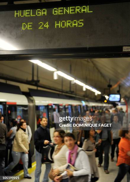 Commuters step out a metro under an electronic board announcing a 24 hours general strike at the Nuevos Ministerios subway station in Madrid on...