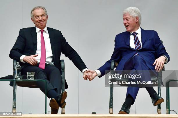 Former US President Bill Clinton holds hands with former British Prime Minister Tony Blair as they attend an event to mark the 20th anniversary of...
