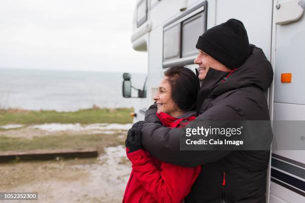 affectionate couple in warm clothing hugging outside motor home - motorhome winter stock-fotos und bilder