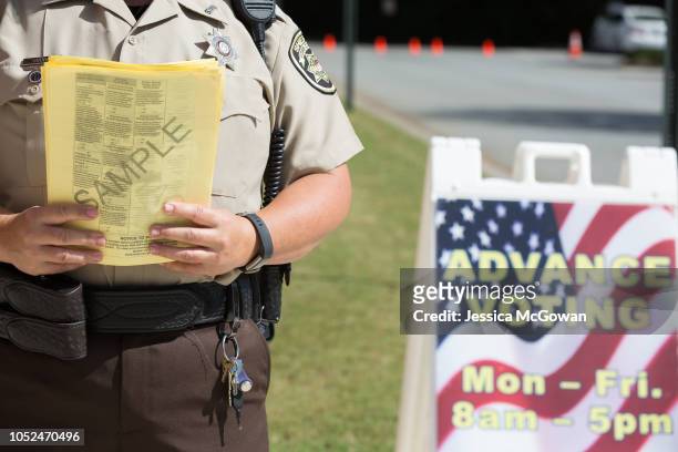 Cobb County Sheriff holds sample ballots outside the Cobb County West Park Government Center where voters line up to early vote on October 18, 2018...