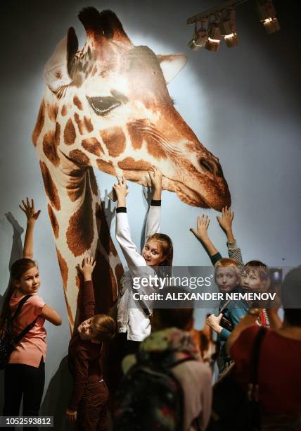Children pose in front of a photograph 'Reticulated Giraffe' by Tim Flach, a British photographer who specialises in studio photography of animals,...