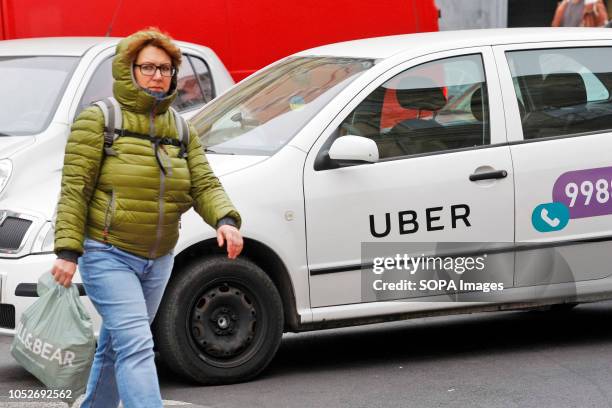Woman seen walking next to a white car with a logo of Uber taxi cab company in Kiev, Ukraine.