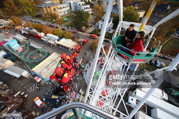 October 2018, Thuringia, Gera: Firefighters practice rescuing people from a gondola on the Ferris wheel at the folk festival. The top gondola of the...