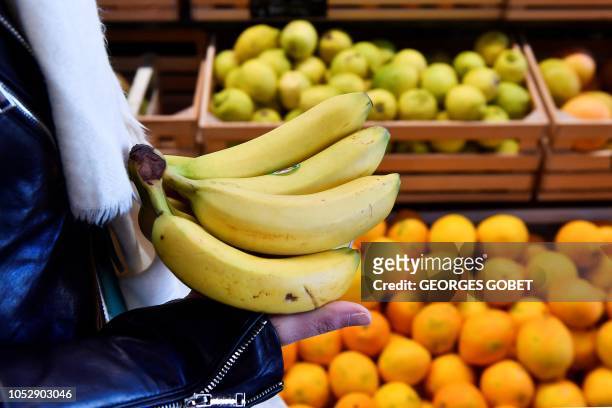 Customer holds bananas in front of a fruit shelf in an organic supermarket in Saintes, western France, on October 23, 2018. According to the public...