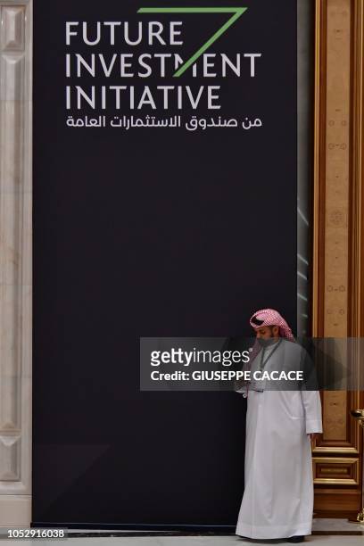 Man looks at his cell phone while walking past a hanging banner bearing the title of the Future Investment Initiative in the Saudi capital Riyadh on...