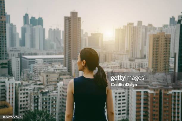 rear view of confident woman overlooking prosperous hong kong city skyline against sky over the top of city at sunrise - corporate skyline stock pictures, royalty-free photos & images