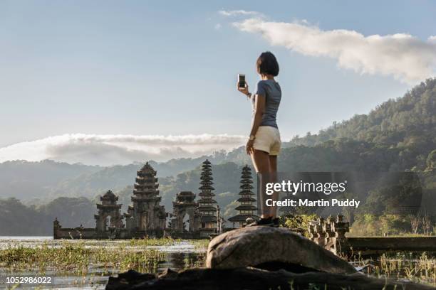 young asian woman, photographing tamblingan temple, using smart phone - rear view photos bildbanksfoton och bilder