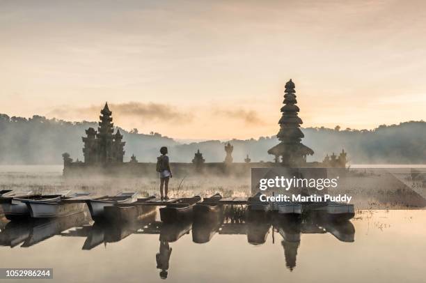 young asian woman standing on boat admiring tamblingan temple - bali travel imagens e fotografias de stock