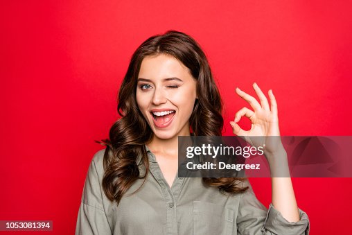 Close up portrait of sweet, gorgeous, nice, adorable, good-looking lady with modern curly hairstyle, casual shirt, show Ok sign and wink isolated on shine red background Close up portrait of sweet, gorgeous, nice, adorable, good-looking lady with modern curly hairstyle, casual shirt, show Ok sign and wink isolated on shine red background