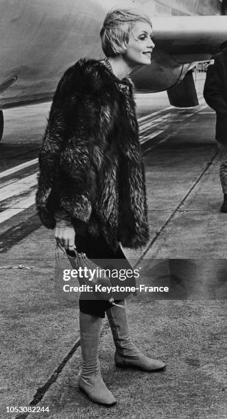 Le mannequin anglais Twiggy vêtue d'un pantalon noir, d'une veste de fourrure et de bottes en daim photographiée à l'aéroport de Londres,...
