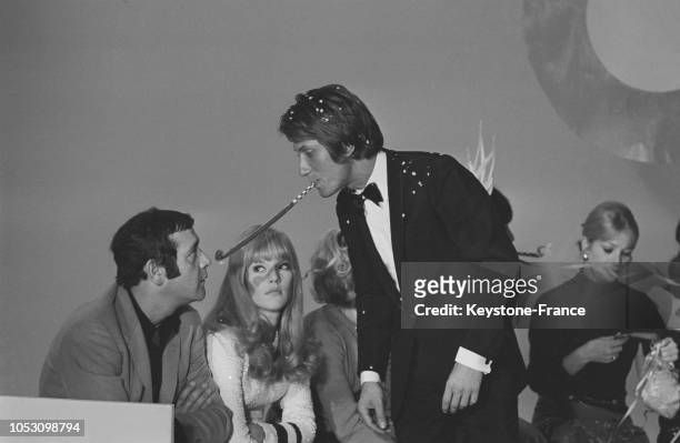 Jacques Dutronc soufflant dans un cotillon devant le visage de Jean Yanne sous le regard de Sylvie Vartan lors du tournage d'un show télévisé, à...
