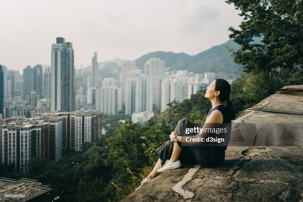 Young woman with eyes closed enjoying the tranquility and the spectacular city skyline on the top of mountain