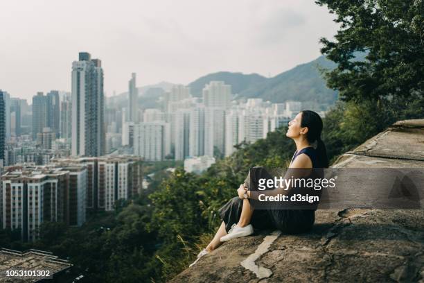 young woman with eyes closed enjoying the tranquility and the spectacular city skyline on the top of mountain - ergens overheen kijken stockfoto's en -beelden