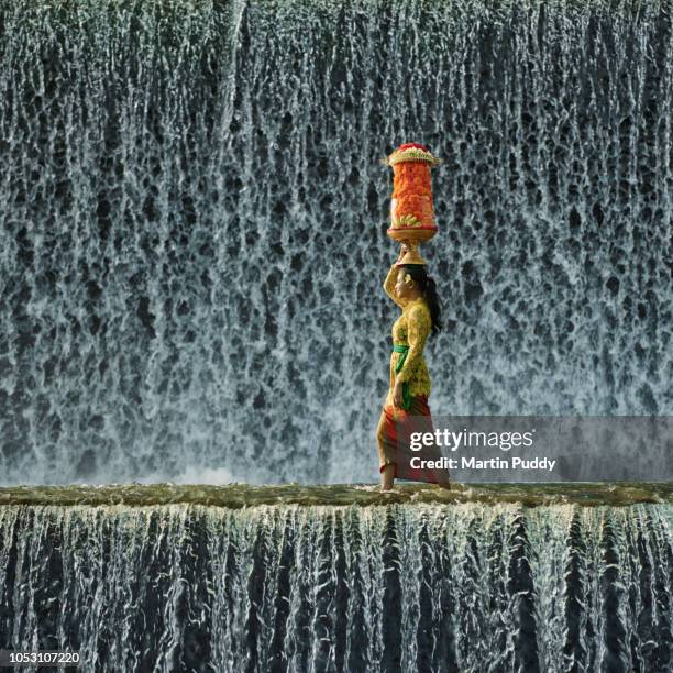 young balinese woman wearing traditional clothing, walking across waterfall - bali waterfall stock pictures, royalty-free photos & images