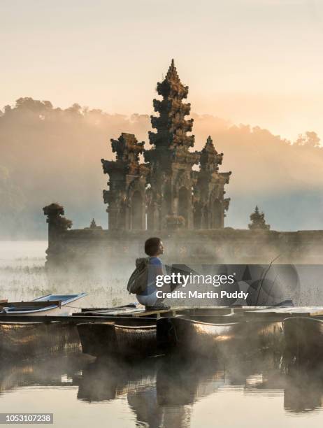 young asian woman sitting on boat admiring tamblingan temple - tourismus stock-fotos und bilder