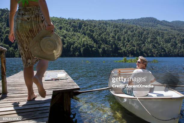 rijpe vrouw ontspant op dok terwijl man rijen boot op lake - pucon stockfoto's en -beelden