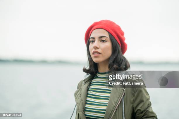 dramatic portrait of a young black-haired woman wearing a beret by the water - ontario canada people stock pictures, royalty-free photos & images