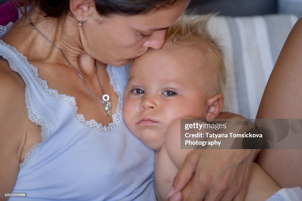 Mother hugging her sick toddler boy, checking his temperature