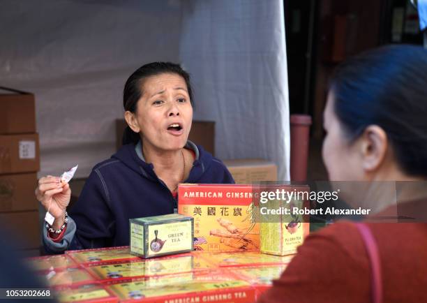 Chinese woman selling American ginseng tea at a street festival makes a sales pitch to a potential customer in Chinatown, San Francisco, California.