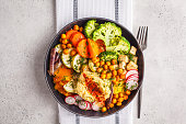 Vegan Buddha bowl with baked vegetables, chickpeas, hummus and tofu, top view.