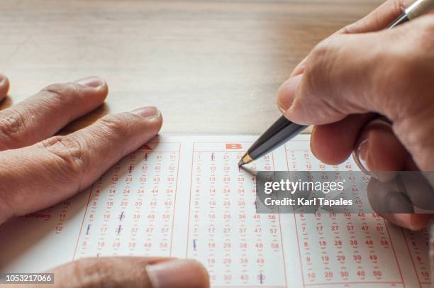 close up of hands filling up a lottery ticket form - lottery tickets photos et images de collection