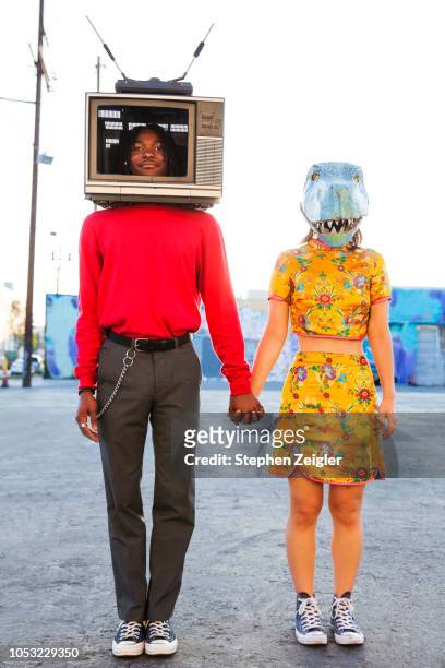 portrait of young man with a television set on his head and a woman wearing a dinosaur mask - bizzarro foto e immagini stock
