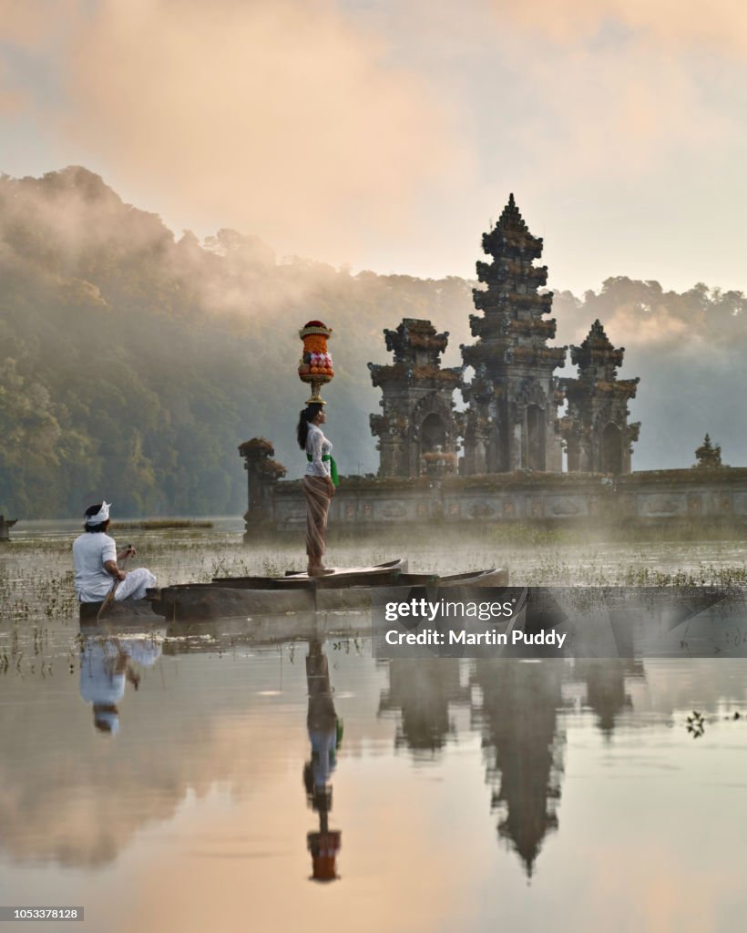 Balinese woman standing on dugout boat looking at Tamblingan temple at sunrise