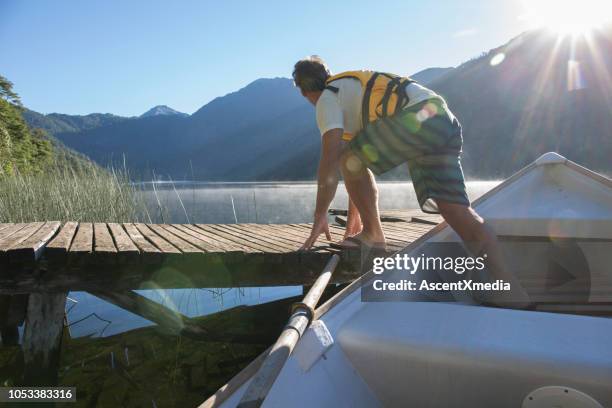 mature man launches rowboat from dock in mountain lake - wood pier stock pictures, royalty-free photos & images