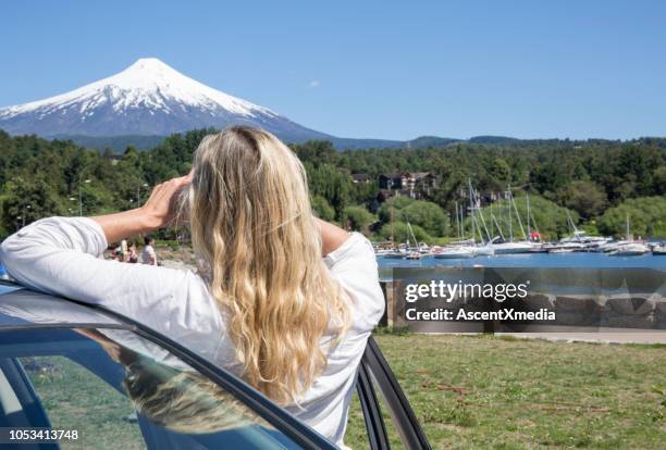 woman leans against car and looks at snow capped volcano - pucon stock pictures, royalty-free photos & images