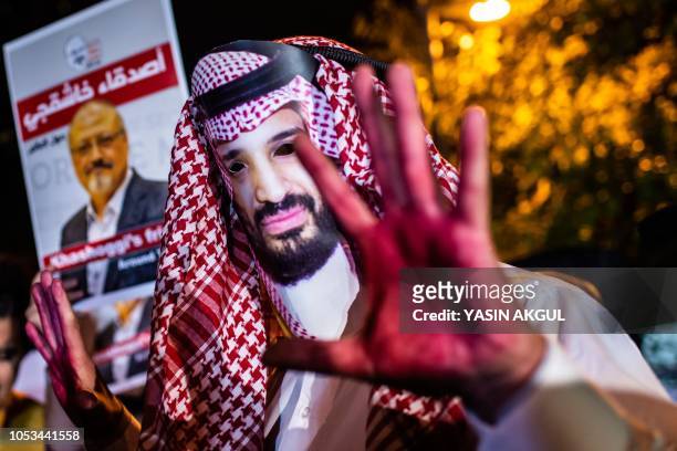 Protestor wears a mask of depicting Saudi Crown Prince Mohammad Bin Salman with red painted hands next to people holding posters of Saudi journalist...