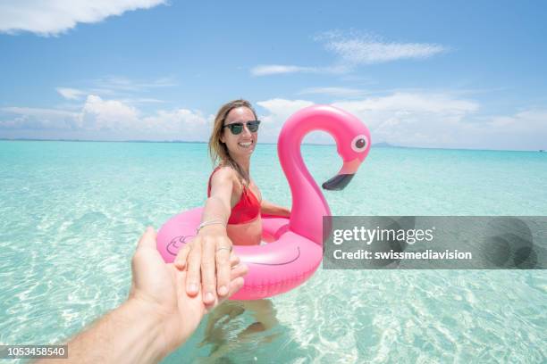 follow me concept woman leading boyfriend on idyllic beach with inflatable flamingo playing in pristine clear water in the islands of thailand. people travel luxury fun and cool attitude concept - follow me stock pictures, royalty-free photos & images