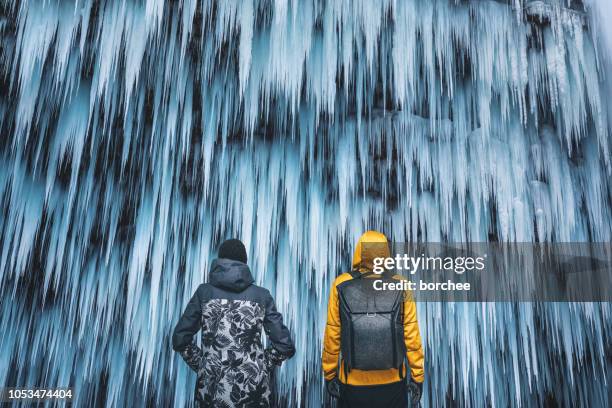 couple admiring the frozen waterfall - yellow coat snow stock pictures, royalty-free photos & images