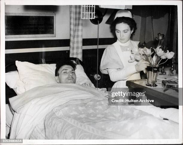 Nurse arranges a vase of tulips for H. Burman of the London Fire Service, who is a patient at the London Hospital which he helped to save during the...