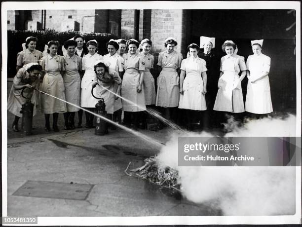 Nurses putting out a fire with the aid of a fire extinguisher, during one of their regular drills under the direction of the NFS , World War II,...