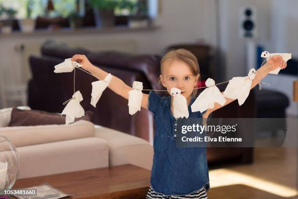 girl (6-7) holding up a string of paper halloween ghosts - halloween deko stock-fotos und bilder