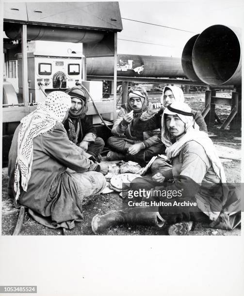 Group of Bedouin Arab artisans, surrounded by the pipe-laying equipment on which they work, eat their mid-day meal at Kirkuk, North Iraq during the...