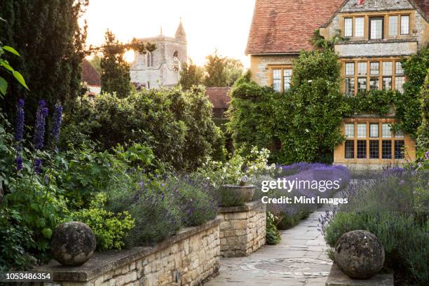 view of historic manor house from across a walled garden with path and flowerbeds. - oxfordshire stock pictures, royalty-free photos & images