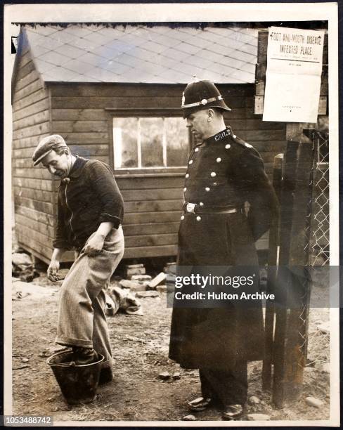 Police guard watching to make sure a worker disinfects his boots as he leaves the Pengam Small Holdings in Glamorgan, South Wales, where an outbreak...