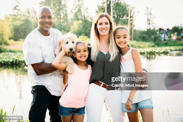 portrait of mixed-race family by lake with labradoodle puppy - interracial wife photos stock pictures, royalty-free photos & images
