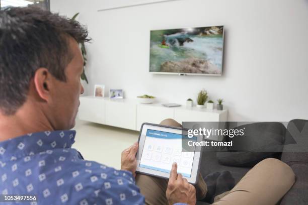 man using smart home automation in living room with digital tablet - adjusting stock pictures, royalty-free photos & images