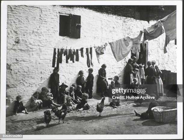 Children and chickens sitting under a washing line hanging across a courtyard in a slum area of London, England, 1889.
