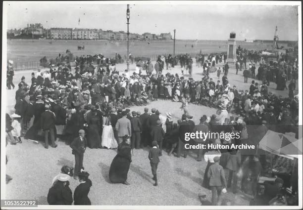 Crowds watching a street performer on the seafront at Southsea, England, 1890s.