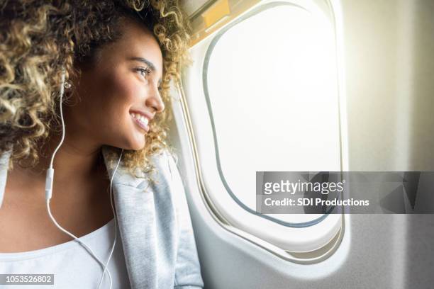 begeistert junge geschäftsfrau genießt fensterplatz bei flugreisen - ohrhörer stock-fotos und bilder