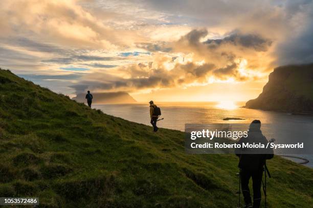 hikers towards drangarnir rock, vagar island - photographer seascape stock pictures, royalty-free photos & images