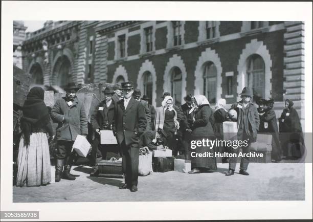 Immigrants, Immigrants stand with trunks outdoors in front of a building on Ellis Island, New York City, Ellis Island, New York City.