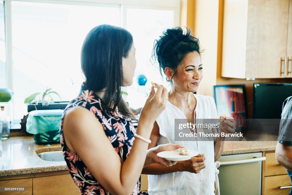 Smiling adult sisters hanging out in kitchen eating lunch