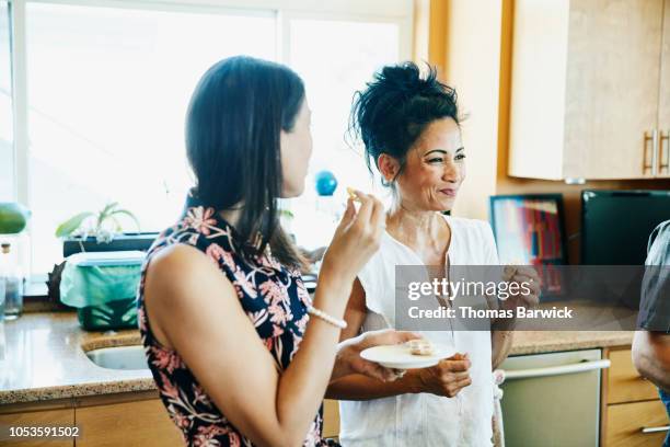 smiling adult sisters hanging out in kitchen eating lunch - 50 year old indian lady stock pictures, royalty-free photos & images